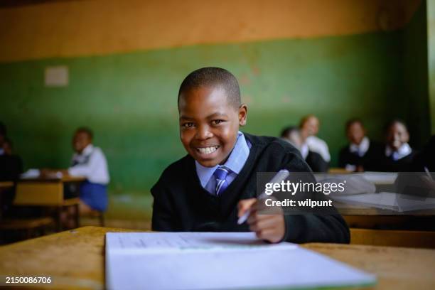 close-up cute schoolboy in uniform sitting in classroom looking at camera smiling - khaki stock pictures, royalty-free photos & images