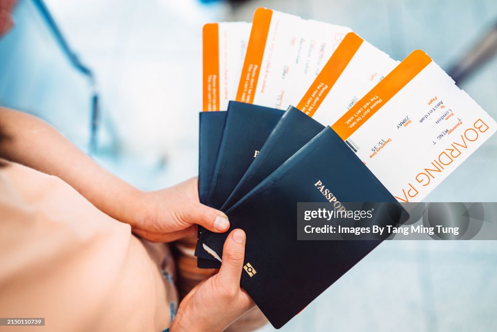 Family Vacation Excitement: Young girl’s hands holding passports & boarding passes of her family while waiting at check-in counter in the airport