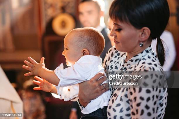 joven madre sosteniendo a su bebé durante el bautizo en la iglesia ortodoxa - bautizo fotografías e imágenes de stock