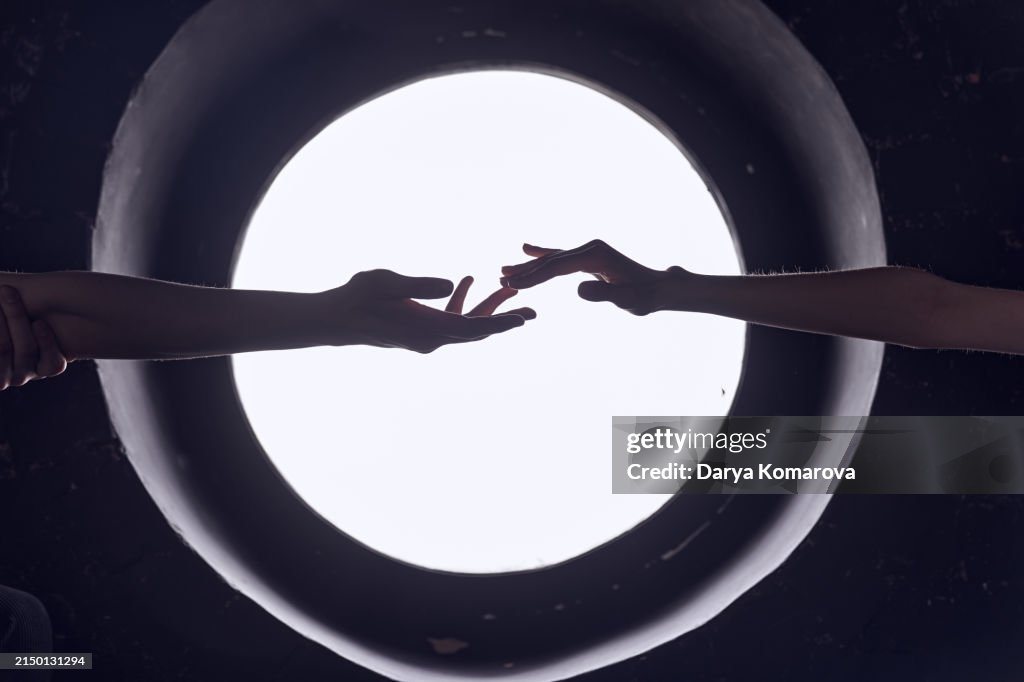 Two hands of a man and a woman reach out to each other against the background of a round window on a black wall. The concept of love and overcoming distances.