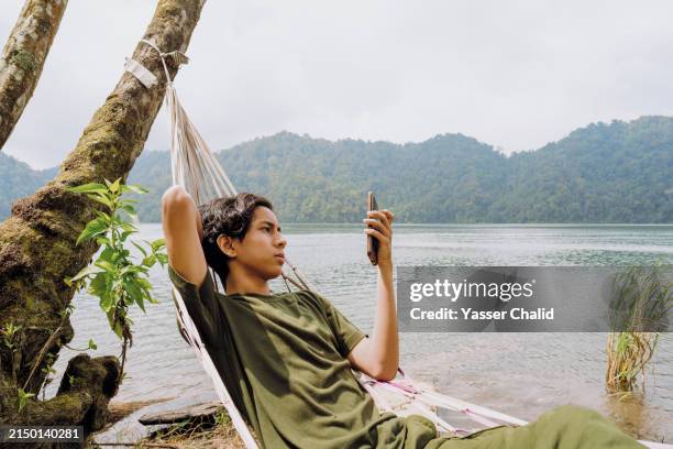 teenager laying on hammock using smartphone - lazy lake stock pictures, royalty-free photos & images