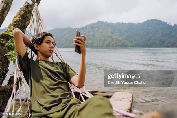 teenager laying on hammock using smartphone - lazy lake stock pictures, royalty-free photos & images