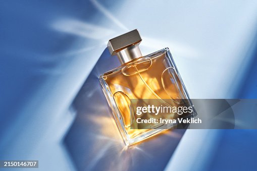 Make-up Cosmetic product for a woman glass bottle Perfume in a glass transparent bottle with caustic Light effect on Blue Color background with shadow from sunlight. Make-up Cosmetic product for a woman glass bottle Perfume in a glass transparent bottle with caustic Light effect on Blue Color background with shadow from sunlight.