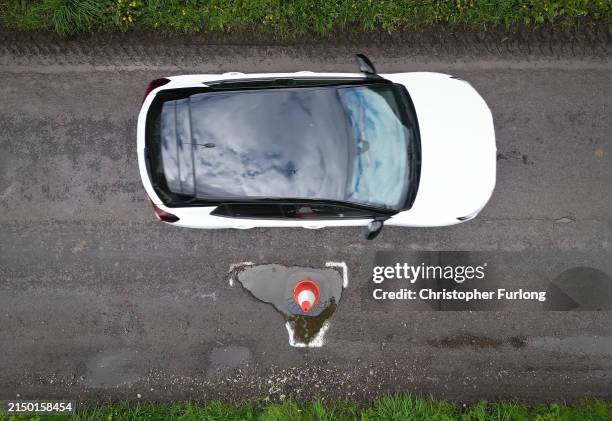 In this aerial view a traffic cone warns drivers of a pothole on the road on April 25, 2024 near Northwich, United Kingdom. The UK's roads have a...