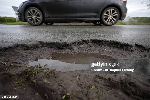 Cars drive past a pothole on the road on April 25, 2024 near Northwich, United Kingdom. The UK's roads have a large number of potholes due to high...