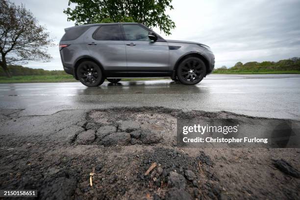 Cars drive past a pothole on the road on April 25, 2024 near Northwich, United Kingdom. The UK's roads have a large number of potholes due to high...