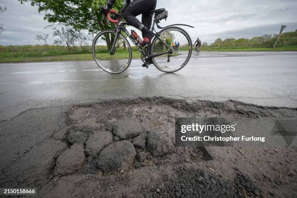 Cyclist rides past a pothole on the road on April 25, 2024 near Northwich, United Kingdom. The UK's roads have a large number of potholes due to high...