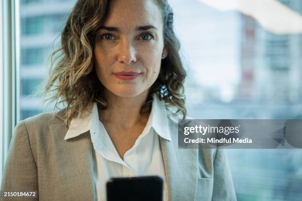 geschäftsfrau schaut in die kamera, während sie ein smartphone hält - halbnahe-einstellung stock-fotos und bilder