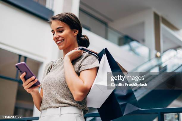 happy woman shopping and using smartphone in modern mall - retail place stock pictures, royalty-free photos & images