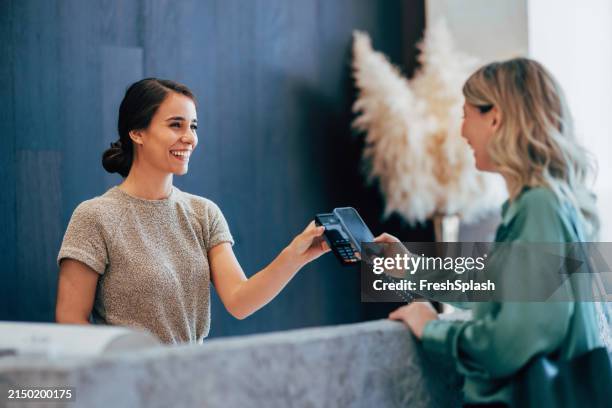 smiling receptionist taking payment at modern hotel desk - boutique stock pictures, royalty-free photos & images