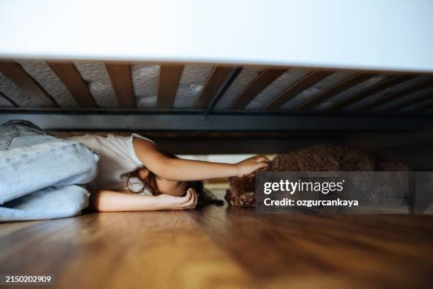 kleiner gilr, der sich unter einem bett versteckt - verängstigt stock-fotos und bilder