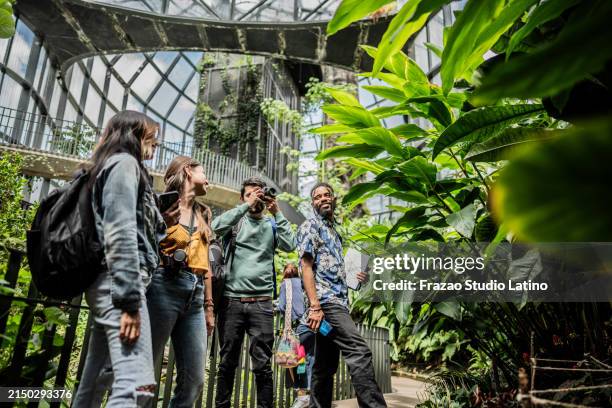 young man taking photos during tour with his friends in the botanical garden - environmentalist stock pictures, royalty-free photos & images