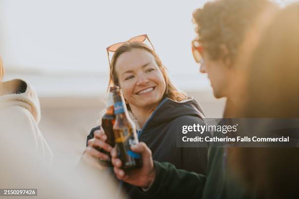 close-up of two people making a toast with beer bottles on the beach - party social event stock pictures, royalty-free photos & images