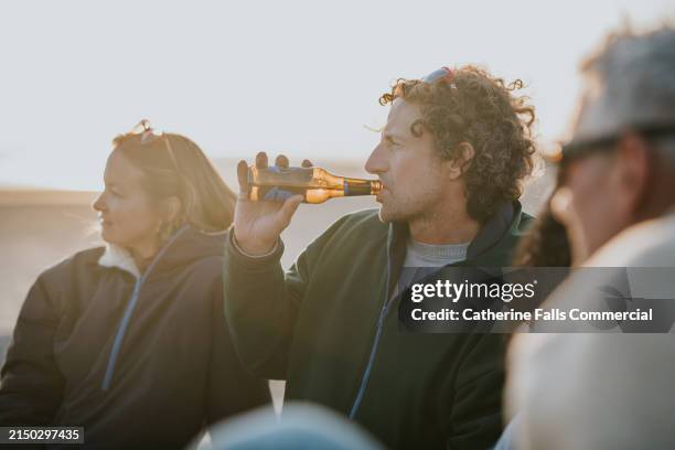 a man drinks beer from a bottle on the beach - beer bottle stock pictures, royalty-free photos & images