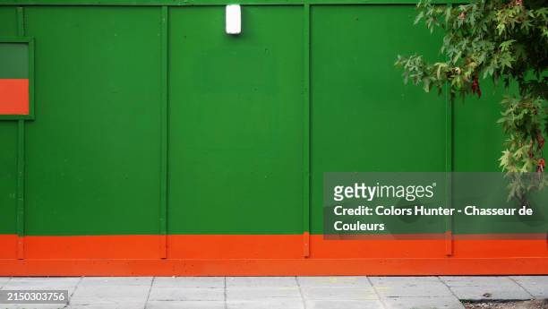 construction site fence made of wooden panels painted green and orange. paved and damaged sidewalk. tree branches.
london, england, united kingdom.
sunlight. natural colors. - retro style wood paneling stock pictures, royalty-free photos & images