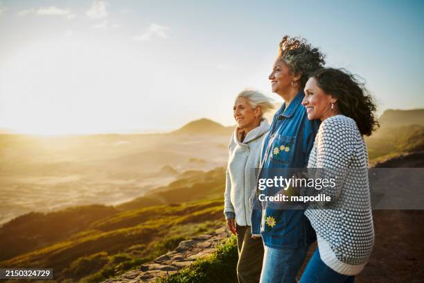 smiling mature friends standing arm in arm by a scenic coast during a road trip - endast kvinnor bildbanksfoton och bilder