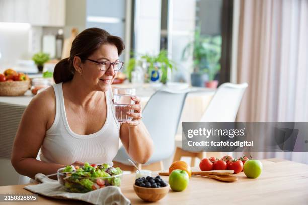 konzept der gesunden ernährung. frau trinkt wasser, während sie eine gesunde mahlzeit aus salat und obst zu sich nimmt - wasser trinken stock-fotos und bilder
