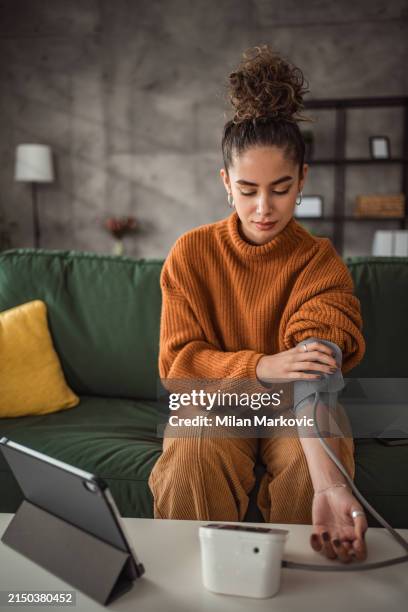 a young woman checks her blood pressure - bloeddrukmeter stockfoto's en -beelden
