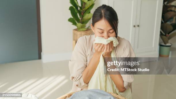 beautiful young asian woman smelling clean clothes and smiling while doing laundry at home. activity of daily living at house. - odorat photos et images de collection