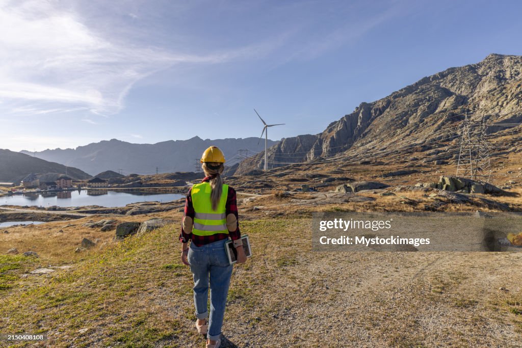 Female engineer conducting an inspection of wind turbines infrastructure for renewable energy production, Using a digital tablet to log data on location