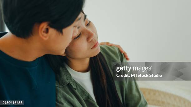 close-up of asian sad man crying while talking and discussing mental health problems with his wife at home. the couple communicates with each other about relationship problems with empathy. - emotional support stock pictures, royalty-free photos & images