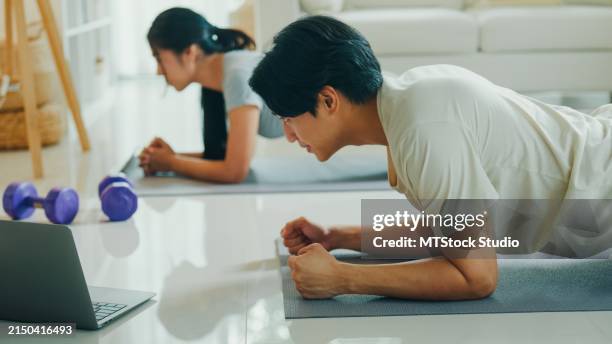 ein fröhliches junges asiatisches paar konzentriert sich darauf, während einer trainingseinheit zu hause nach einem online-kurs eine plank-position zu halten. genießen sie das fitnesstraining zu hause. - fitnessraum stock-fotos und bilder