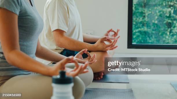 gros plan d’un jeune couple asiatique serein et joyeux médite dans la position du lotus dans un cadre domestique paisible, avec un ordinateur portable à proximité pour une méditation guidée. profiter de l’entraînement physique à domicile. - tapis de sol photos et images de collection