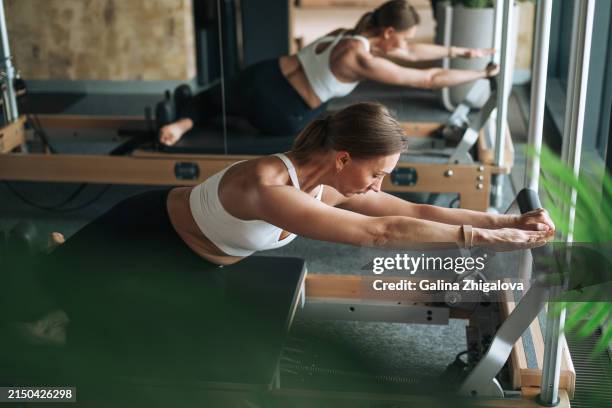 young adult slim woman in sportswear doing pilates on reformer in modern studio - metodo pilates foto e immagini stock