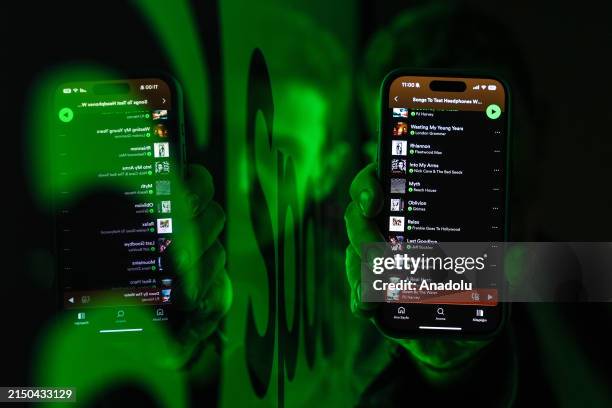 In this photo illustration a man wearing smart glasses holding a mobile phone displaying the Spotify song list near the board with Spotify icon in...