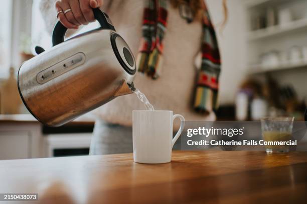 a woman pours boiling water from a modern chrome kettle into a white mug - kaffekanna bildbanksfoton och bilder
