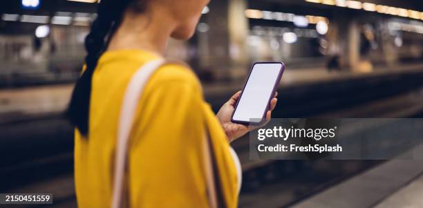 young woman holding smartphone at train station at night - blank screen stock pictures, royalty-free photos & images