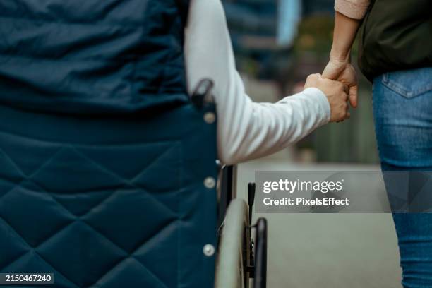 hombre discapacitado en silla de ruedas y mujer cogida de la mano - dar una mano fotografías e imágenes de stock