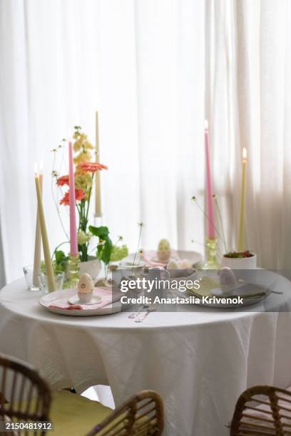 setting table for easter dinner with candles, flowers, multicolored eggs and ceramic plates. - easter breakfast stock pictures, royalty-free photos & images