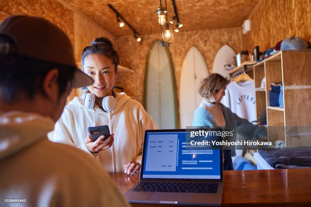 Mature woman making contactless payment using smartphone at shop checkout counter by the Pacific Ocean.