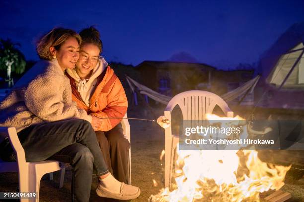 mature women roasting marshmallow on bonfire and cheek to cheek. - burns night stock pictures, royalty-free photos & images