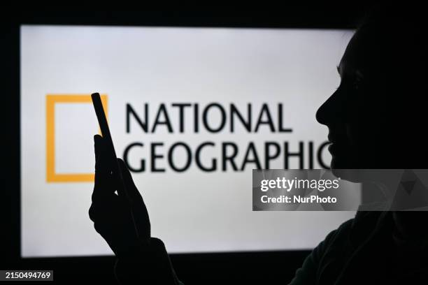 An image of a woman holding a cell phone in front of the National Geographic logo displayed on a computer screen, on April 29 in Edmonton, Canada.