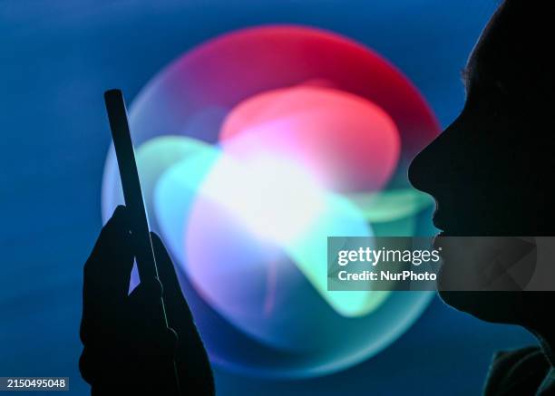 An image of a woman holding a cell phone in front of the Siri logo displayed on a computer screen, on April 29 in Edmonton, Canada.