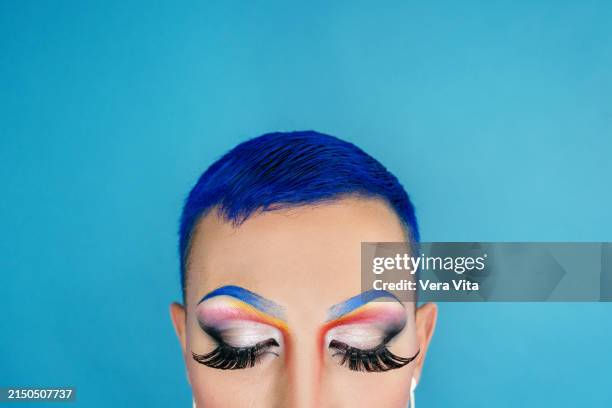 close up portrait of young man with make up isolated on blue background - maquillaje para ojos fotografías e imágenes de stock