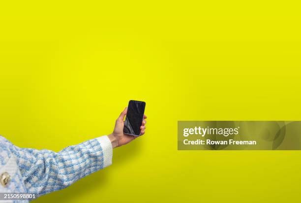 womans hand holding phone in smart clothing against a yellow background - photo messaging stock pictures, royalty-free photos & images