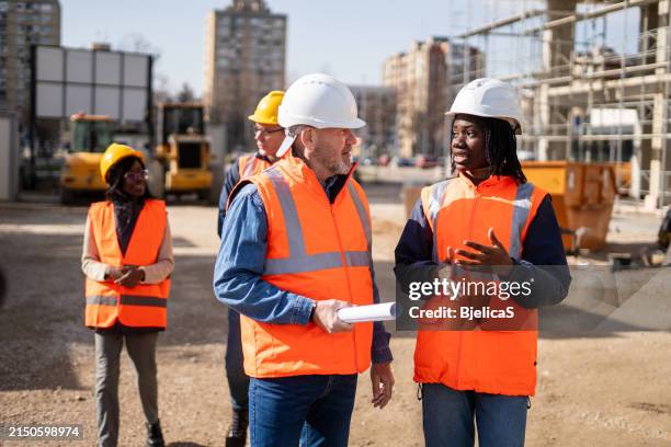 multiracial construction workers talking at construction site - walking with reflective clothing stock pictures, royalty-free photos & images