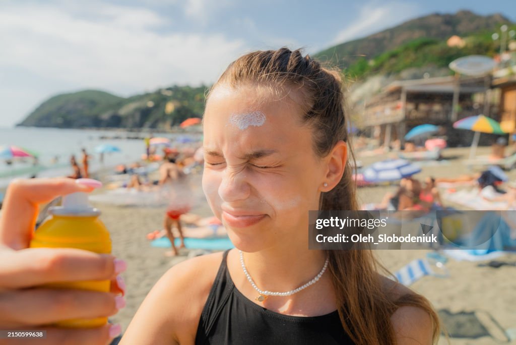 Girl spraying sunscreen on her face on beach vacation