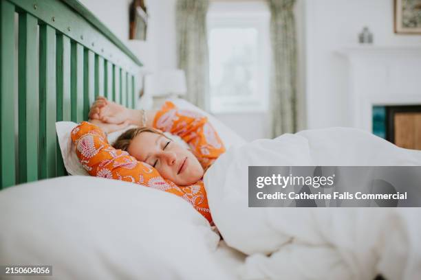 a young woman in orange pyjamas is fast asleep in a double bed - slapen stockfoto's en -beelden