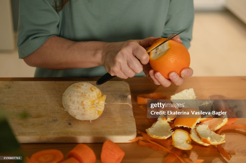Woman peeling an orange at the kitchen table at home. Hands close up