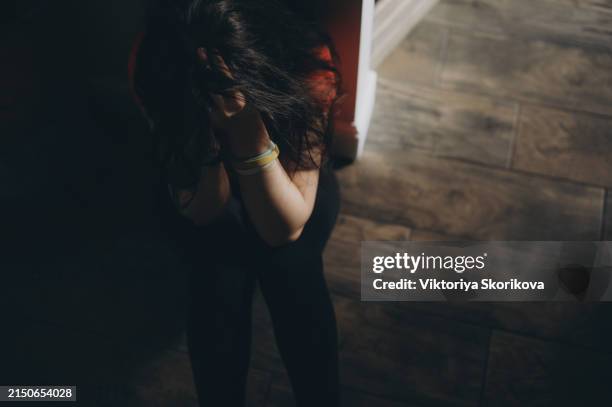 upset teen girl sit on floor sadly look out window worried about teenage problem at school and communication with parent. worried girl tensely suffer about bullying at school, unrequited love with boy - violencia fotografías e imágenes de stock