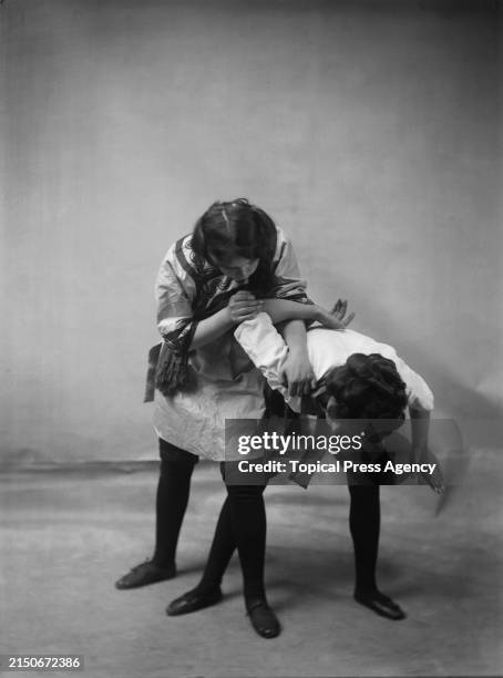 British martial artist and suffragette Edith Garrud demonstrating a jiu-jitsu hold on a young woman, circa 1910. Both women are wearing gi jackets...