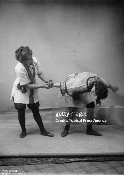 British martial artist and suffragette Edith Garrud demonstrating a jiu-jitsu hold on a young woman, circa 1910. Both women are wearing gi jackets...