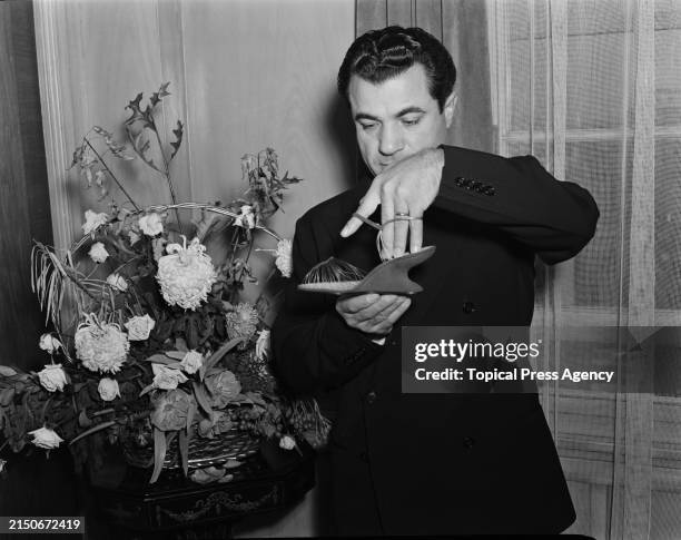 Italian shoe designer Salvatore Ferragamo holding an 'Invisible' wedge sandal from his 1947 collection during a visit to the United Kingdom, October...