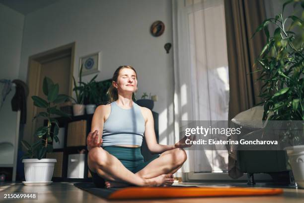 woman enjoys a peaceful moment in meditation, embraced by the warmth of her home. - budismo imagens e fotografias de stock