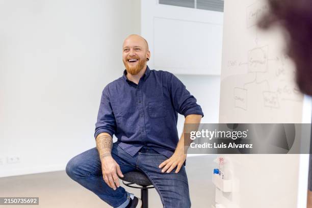software engineer sitting by whiteboard and smiling during meeting at startup - data scientist stock pictures, royalty-free photos & images