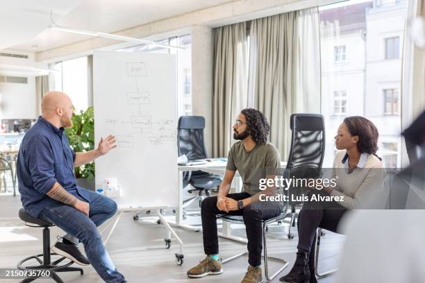 startup entrepreneur talks about app development while pointing at a whiteboard during meeting - hair colour stock pictures, royalty-free photos & images